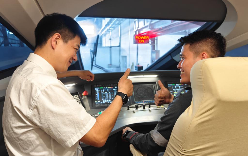 8月25日，在印度尼西亞萬隆的雅萬高鐵德卡魯爾動車所內(nèi)，中國師傅穆振（左）在向印尼火車司機塞蒂亞萬講解動車組出庫前的上電作業(yè)。