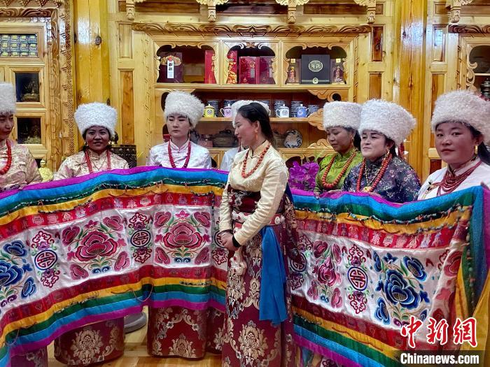 圖為女性展示村民自發(fā)繡制的“百米五彩哈達(dá)”?！±钣穹?攝